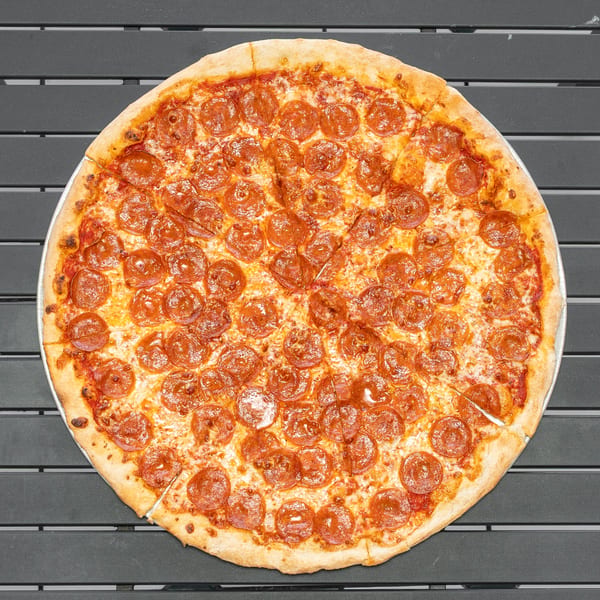A whole pepperoni pizza, cut into slices, rests on a dark gray slatted table.