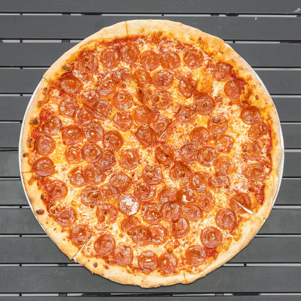 A whole pepperoni pizza, cut into slices, rests on a dark gray slatted table.
