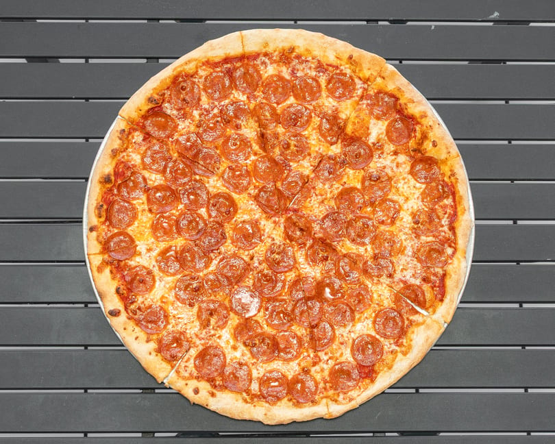 A whole pepperoni pizza, cut into slices, rests on a dark gray slatted table.