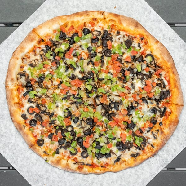 Whole vegetarian pizza with black olives, green peppers, onions, and tomatoes on parchment paper.