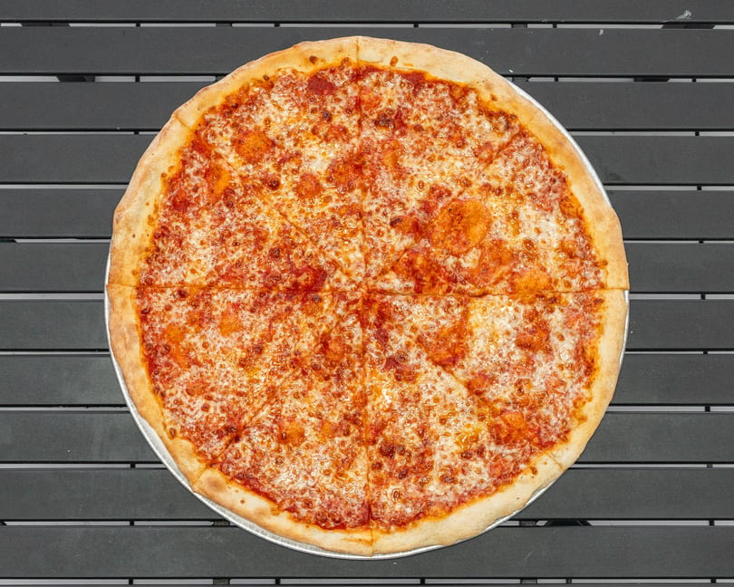 A whole cheese pizza, cut into eight slices, on a dark gray slatted table.