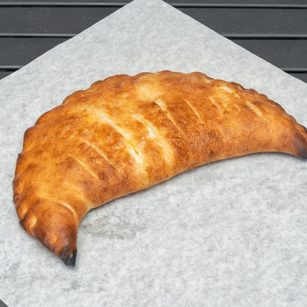 Golden-brown calzone with diagonal cuts on parchment paper, against a dark background.