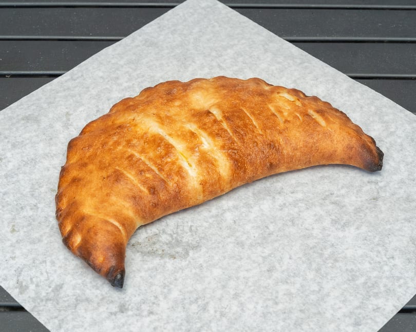 Golden-brown calzone with diagonal cuts on parchment paper, against a dark background.